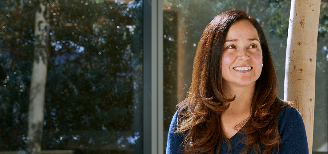 مونتسي تبتسم وتجلس بالقرب من نافذة كبيرة مشمسة، وهناك أشجار في الخلفية.