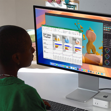 Woman working on an Excel spreadsheet on a Mac, sitting at a work table. The Excel spreadsheet is a Q4 sales tracker. Behind the Excel spreadsheet window is a Pixelmator Pro window.