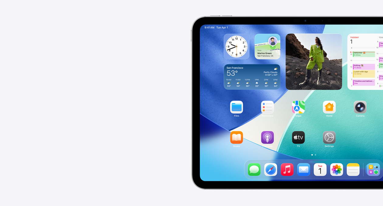 iPad, orientasi lanskap, sisi kiri layar saja, Layar Utama dengan susunan widget yang meliputi jam tembus cahaya yang menampilkan efek Liquid Glass, aplikasi Lacak, widget Cuaca, dua baris aplikasi yang lebih kecil, dan dock