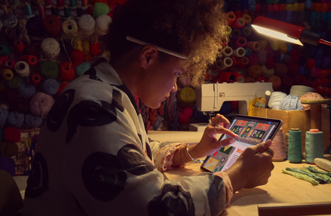 A person sitting at a desk uses two fingers on the screen of an iPad to zoom in on an image.