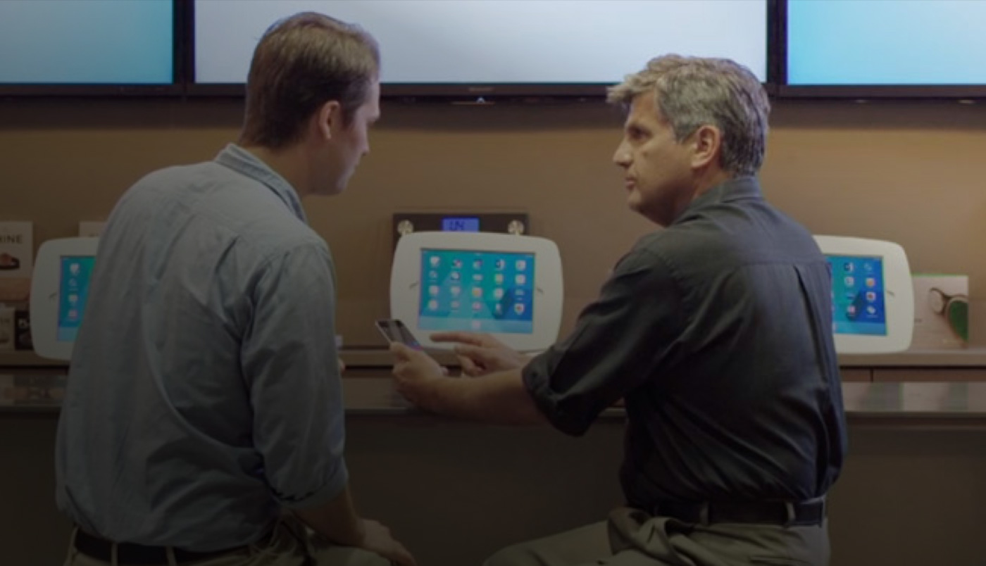 Dois homens sentados em O Bar, olhando para a tela de um iPhone.