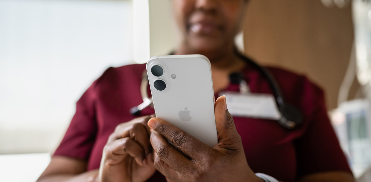 A female nurse in red scrubs looks at her iPhone.