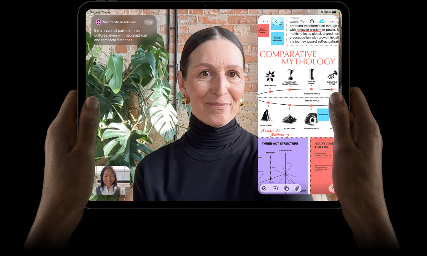 Vista frontal do iPad Pro, preto sideral, mãos a segurar os lados esquerdo e direito do dispositivo na horizontal, ecrã com moldura preta e cantos arredondados, o ecrã apresenta uma conversa no FaceTime com tradução em tempo real e uma app educativa com uma apresentação intitulada "Mitologia Comparativa" com texto, diagramas e notas escritas à mão